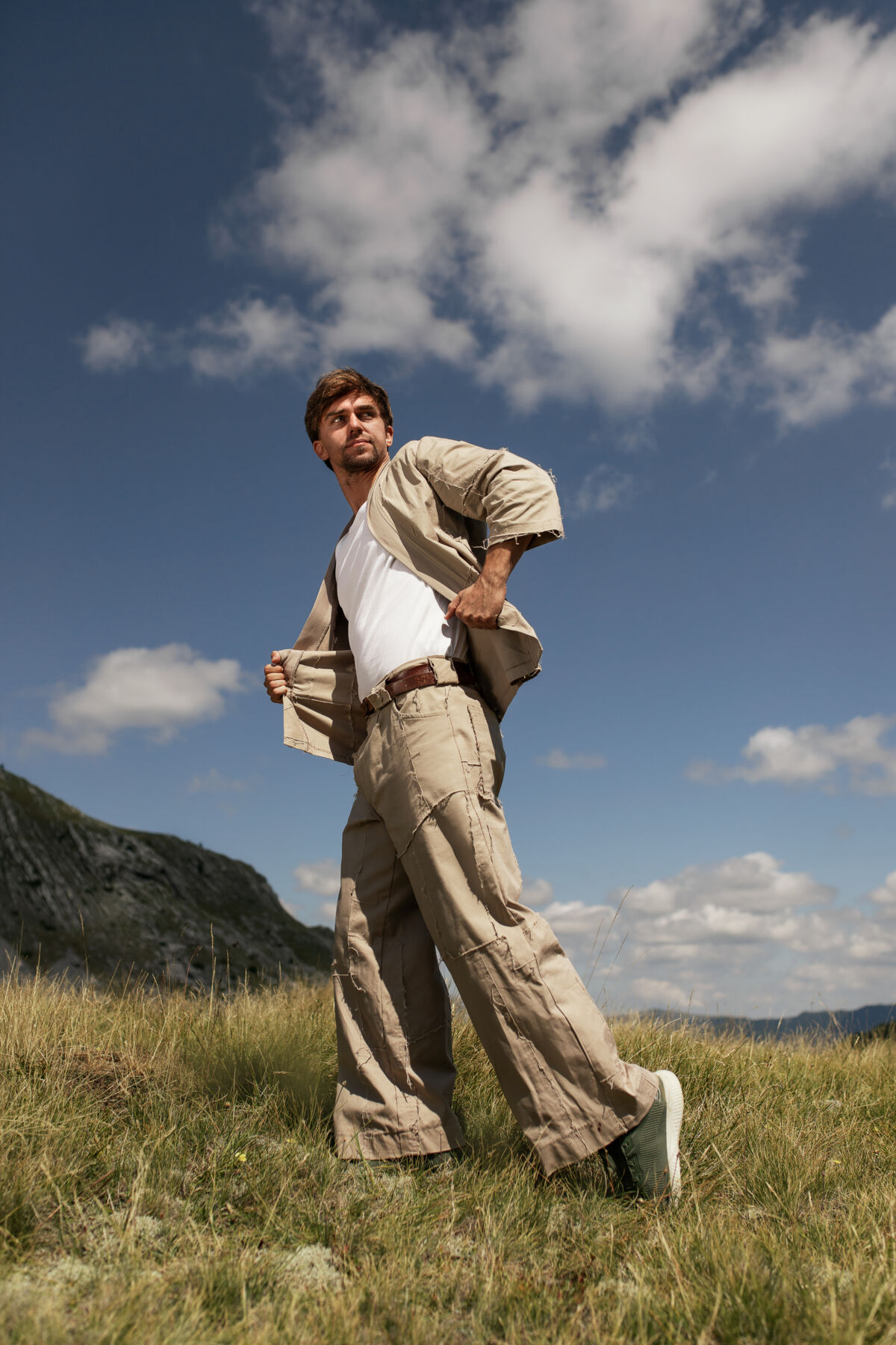 Filip Radovanović u bež kimono kompletu na livadi, oblaci u pozadini — Free Spirit muška moda