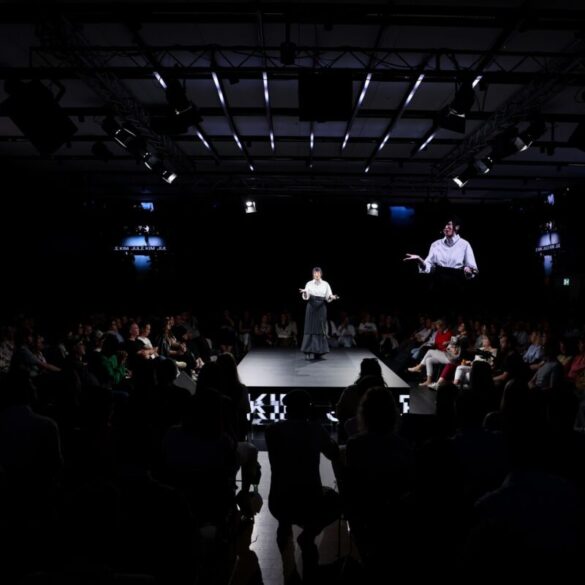 Govornica na dugačkoj catwalk pozornici okruženoj publikom s obje strane i četiri velika ekrana s njezinim likom, u tamnoj dvorani Dana komunikacija 2026.