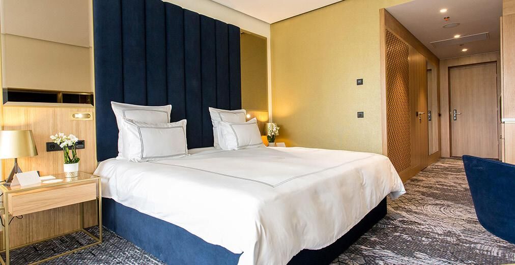 NovaAmbienta hotelska soba tamno plavi tapaciran uzglavlje toplo drvo elegantni detalji