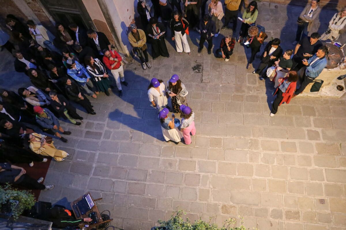 Pogled s balkona na performans kolektiva Border Disorder ispred Palazzo Malipiera — izvođačice s ljubičastim kapama u centru, publika vernisaža raspoređena duž obje strane calle, Venecija, 8. maja 2026.