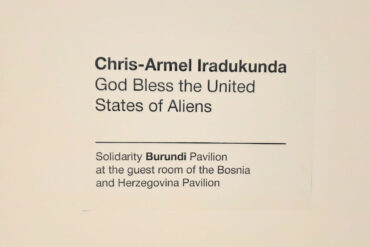 Zidna natpisna pločica s imenom umjetnika i nazivom rada: Chris-Armel Iradukunda, God Bless the United States of Aliens — Solidarity Burundi Pavilion at the guest room of the Bosnia and Herzegovina Pavilion, Palazzo Malipiero, Venecija 2026.