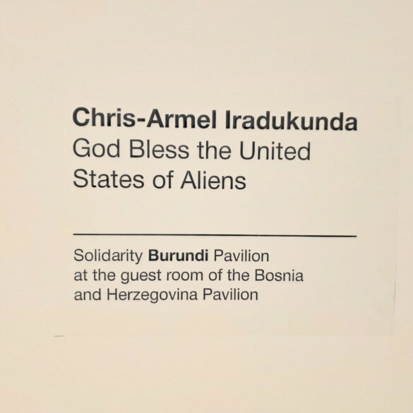 Zidna natpisna pločica s imenom umjetnika i nazivom rada: Chris-Armel Iradukunda, God Bless the United States of Aliens — Solidarity Burundi Pavilion at the guest room of the Bosnia and Herzegovina Pavilion, Palazzo Malipiero, Venecija 2026.