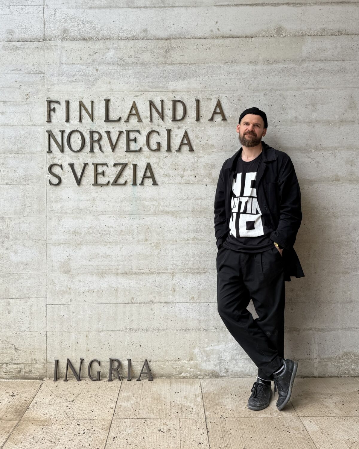 Pavel Rotts stoji uz betonski zid Nordijskog paviljona u Veneciji ispod natpisa Finlandia, Norvegia, Svezia, a pri dnu zida složena su tamna metalna slova koja čine riječ INGRIA.