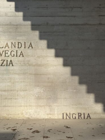 Vanjski betonski zid Nordijskog paviljona s natpisima Finlandia, Norvegia, Svezia u gornjem lijevom uglu i riječju INGRIA postavljenom pri dnu desno, dok geometrijska sjena stepenica dijeli zid na osvjetljeni i zatamnjeni dio.
