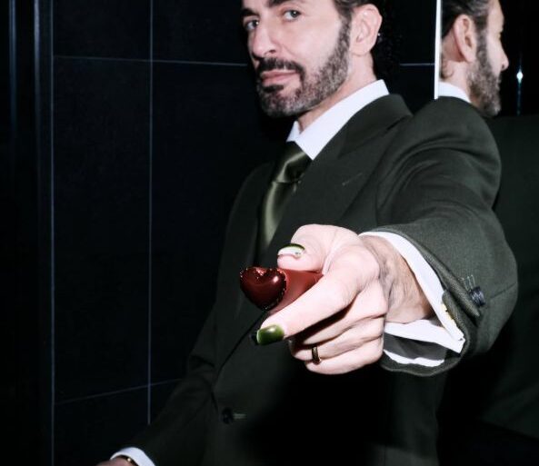 Marc Jacobs u tamnozelenom odijelu pruža maleno srce prema kameri, s odrazom u ogledalu u pozadini — fotografija s njegovog Instagram profila @themarcjacobs