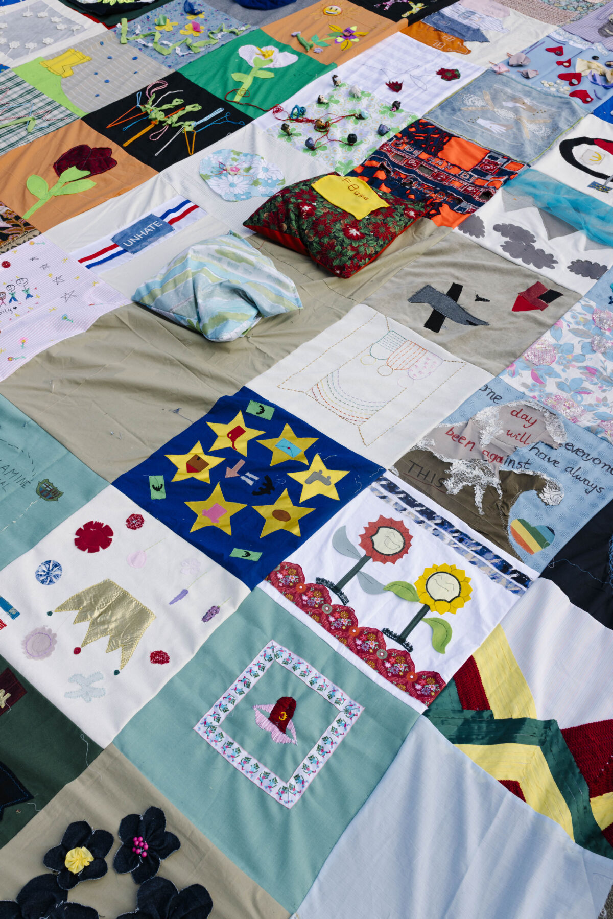 Detaljan pogled na mozaik kolektivnog tekstilnog djela TexTiles — šarene ručno izrađene pločice s motivima zvjezdica EU, suncokreta, cvijeća i natpisom "UNHATE", raspoređene na platnu na podu, Maastricht 2026.