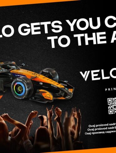 VELO nagradni konkurs – McLaren F1 bolid u narandžasto-crnim bojama s VELO logom, uz slogan "VELO Gets You Closer to the Action" i QR kod za učešće u nagradnom takmičenju za vikend u Monzi. Samo za 18+.
