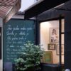 Vanjski izgled galerije Mezzanin na Ferhadiji 16 u Sarajevu, sa zelenom tablom ispisanom stihovima i izloženim radovima u izlogu