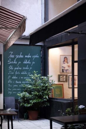 Vanjski izgled galerije Mezzanin na Ferhadiji 16 u Sarajevu, sa zelenom tablom ispisanom stihovima i izloženim radovima u izlogu