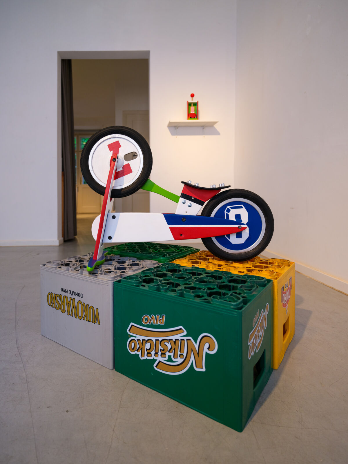 Skulptura Željka Beljana u obliku bicikla s motivima pivskih flaša, postavljena na gajbama za pivo, izložba "Pravo u stolarij", Galerija Manifesto