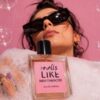 Martimex parfimerija - žena drži bočicu Smells Like Main Character parfema okružena mehurićima na roza pozadini