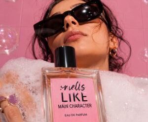 Martimex parfimerija - žena drži bočicu Smells Like Main Character parfema okružena mehurićima na roza pozadini
