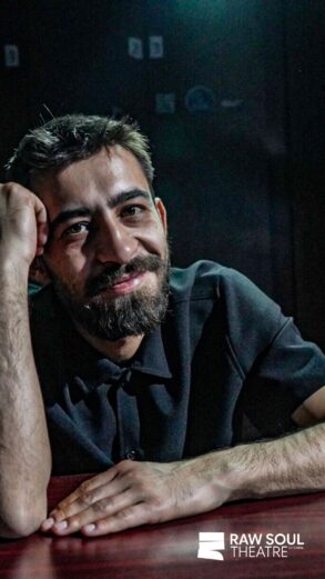 Irfan Ribić, osnivač i umjetnički direktor RAW SOUL THEATRE, naslonjen na sto u zatamnjenom prostoru teatra