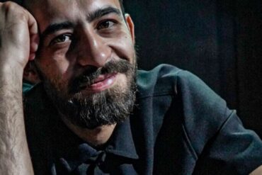 Irfan Ribić, osnivač i umjetnički direktor RAW SOUL THEATRE, naslonjen na sto u zatamnjenom prostoru teatra