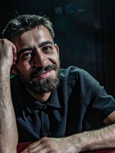 Irfan Ribić, osnivač i umjetnički direktor RAW SOUL THEATRE, naslonjen na sto u zatamnjenom prostoru teatra
