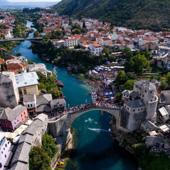 Ptičja perspektiva Starog mosta i rijeke Neretve tokom Red Bull Cliff Diving takmičenja u Mostaru, s dva paraglajdera iznad vode i mnoštvom posjetitelja na obali