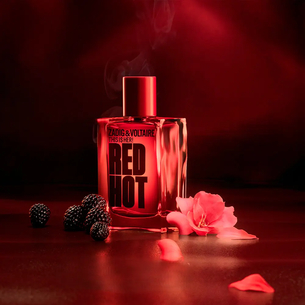 Zadig & Voltaire Red Hot parfem u crvenoj staklenoj bočici okružen kupinama i laticama ruže na tamnoj podlozi