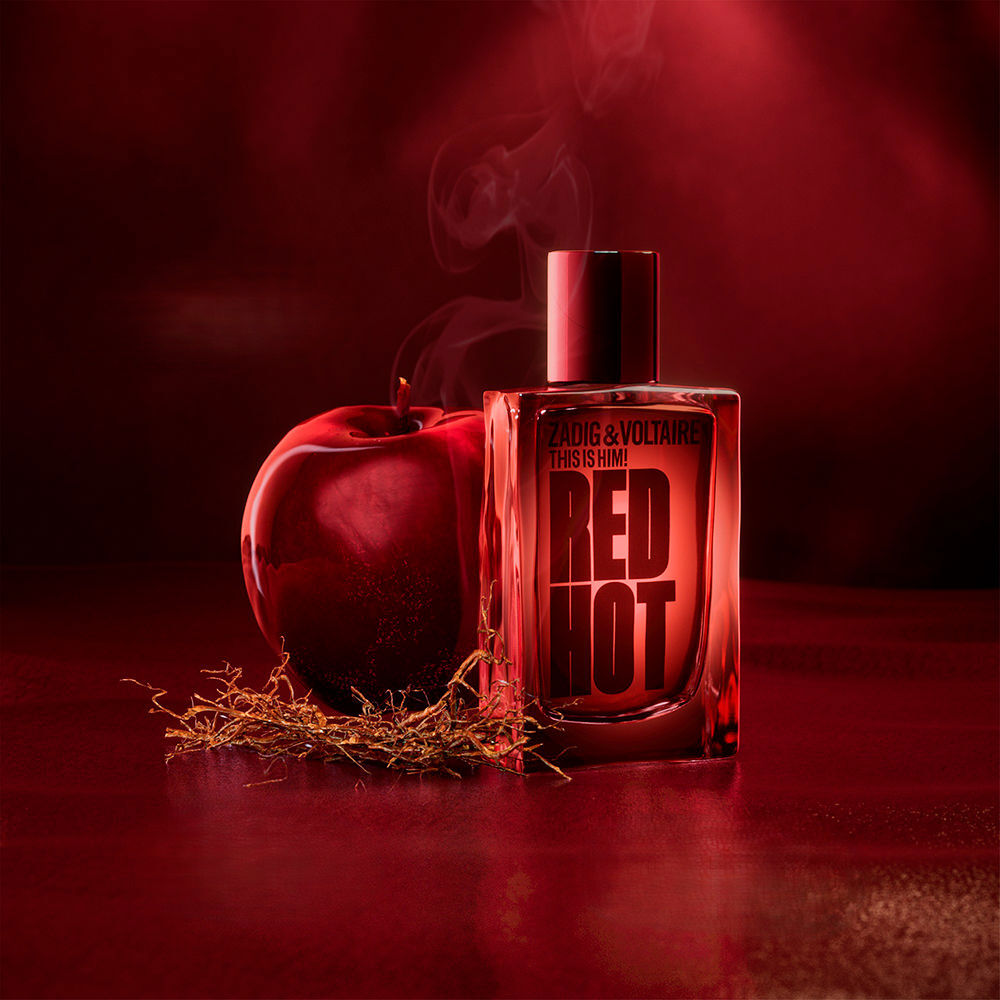 Zadig & Voltaire This Is Him! Red Hot – muški parfem u crvenoj bočici pored crvene jabuke i duhana na tamnocrvenoj podlozi
